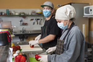 Two young chefs slicing vegetables wearing medical masks